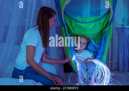 Enfant et thérapeute dans la chambre stimulante sensorielle, snoezelen. Enfant autiste qui interagit avec des lumières colorées pendant la séance de thérapie. Banque D'Images