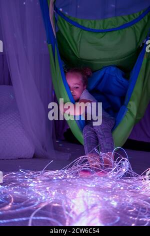 Enfant en salle de thérapie stimulante sensorielle, snoezelen. Enfant autiste qui interagit avec des lumières colorées pendant la séance de thérapie. Banque D'Images