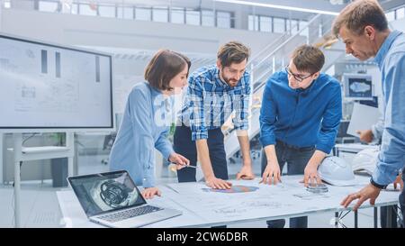 Dans l'usine d'ingénierie industrielle : divers groupes d'ingénieurs et de techniciens réunis autour d'une table avec Engine Design Technical Banque D'Images