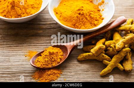 Poudre curcuma jaune et racines sèches sur fond de bois. Banque D'Images