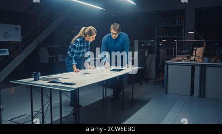 Dans le Dark Industrial Design Engineering Facility mâle et femelle Les ingénieurs travaillent sur des modèles et des dessins techniques à l'aide de la conférence Tableau Banque D'Images