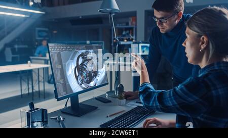 Ingénieur travaillant sur un ordinateur de bureau, écran montrant le logiciel de CAO avec le modèle 3D de moteur, son chef de projet masculin explique les caractéristiques du poste. Industriel Banque D'Images