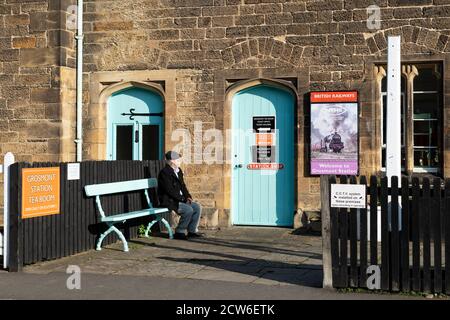 Grosmont Station, North Yorkshire, Angleterre, Royaume-Uni - homme âgé assis sur le banc au soleil devant la boutique, un salon de thé Banque D'Images