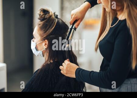 Femme dans le masque médical obtient ses cheveux fait dans la beauté salon pendant une pandémie Banque D'Images