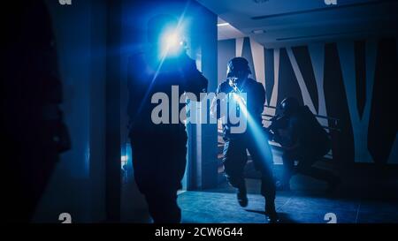 Une équipe masquée d'officiers de police SWAT armés sort de l'ascenseur et tempête le couloir d'un immeuble de bureaux. Soldats avec fusils et Banque D'Images