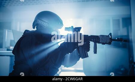 Gros plan Portrait d'un membre masqué de la police SWAT armée qui tempête un immeuble de bureaux sombre saisi avec des bureaux et des ordinateurs. Soldats avec Banque D'Images