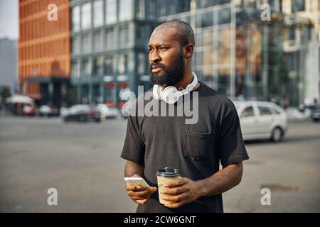 Homme barbu calme dans la ville avec gadget et café Banque D'Images