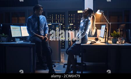 Tard dans la nuit dans le bureau de l'entreprise deux jeunes professionnels discutant amical, échanger des nouvelles, parler d'emploi, flirter Banque D'Images