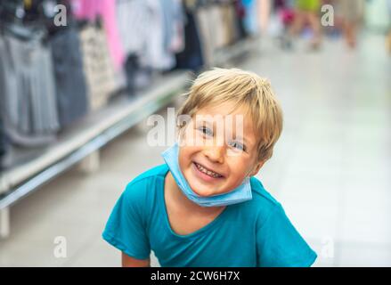 Gros portrait mignon sourire bleu yeux rouillés blond clair garçon expressions artistiques du visage, gestes portant masque hygiénique shopping supermarché. Nouveau Banque D'Images