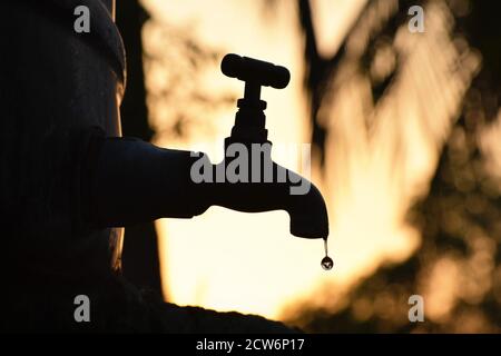 Silhouette de vieux vieux vieux robinet de métal défectueux fuite de goutte d'eau en été sec matin/soir, pénurie d'eau, crise, pénurie, désert, été Banque D'Images