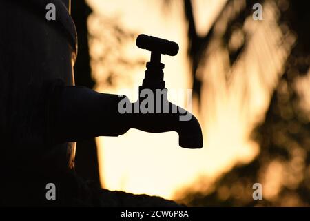 Silhouette de vieux robinet/robinet en métal vintage seul dans un environnement naturel extérieur pendant l'heure dorée du lever du soleil, manque d'eau, beau papier peint Banque D'Images