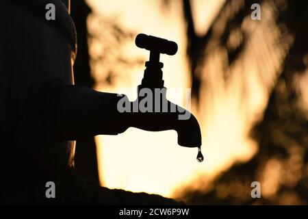 Silhouette de l'ancien robinet de métal vintage qui fuit la dernière goutte d'eau. Seul dans l'environnement naturel extérieur, heure dorée de lever du soleil, pénurie d'eau, crise Banque D'Images