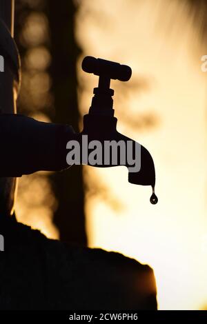 Vertical / portrait-orienté, silhouette de l'ancien robinet en métal vintage goutte d'eau. Seul dans un environnement naturel extérieur pendant l'heure d'or Banque D'Images