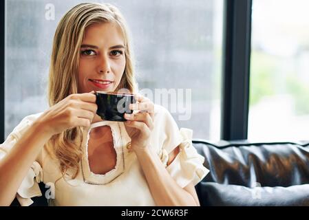 Portrait d'une jeune femme souriante et attirante qui apprécie une tasse de chaleur café noir Banque D'Images