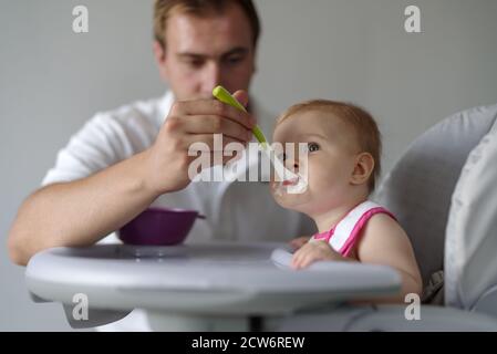 Père nourrissant bébé fille avec une cuillère dans une chaise haute Banque D'Images