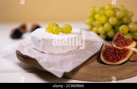 Fromage Camembert sur bois, branche de raisin vert, tranche de figues et noix. Banque D'Images