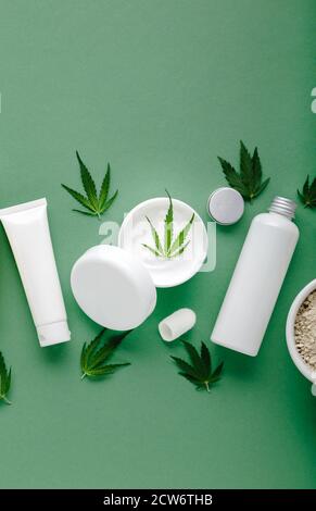 Crème hydratante de chanvre en pot blanc avec de l'huile de CBD cannabis feuilles et mettre en place les cosmétiques de soin de la peau dans des tubes de bouteilles blanches sur fond vert Banque D'Images