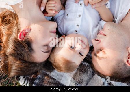 Maman, papa et petit fils allongé sur la couverture dans le parc d'été. Le concept des vacances d'été. Fête de la mère, du père, du bébé. La famille passe du temps Banque D'Images