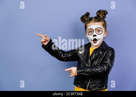 Portrait d'une petite fille mignonne avec un maquillage brillant effrayant, habillé en cuir noir veste, points de côté sur le violet studio copie espace, montre la place de Hallo Banque D'Images