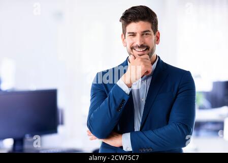 Homme d'affaires réussi portant une chemise et un blazer tout en se tenant au bureau. Banque D'Images