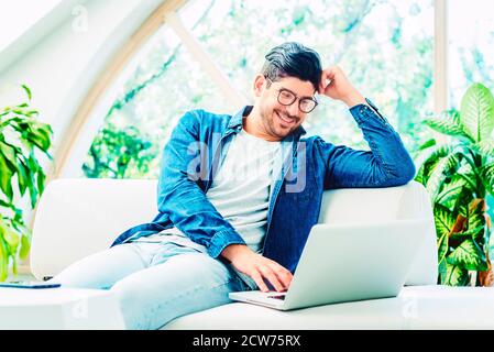 Un homme heureux portant des vêtements décontractés tout en se relaxant sur un canapé et en utilisant un ordinateur portable. Un homme d'affaires qui travaillait chez lui. Banque D'Images