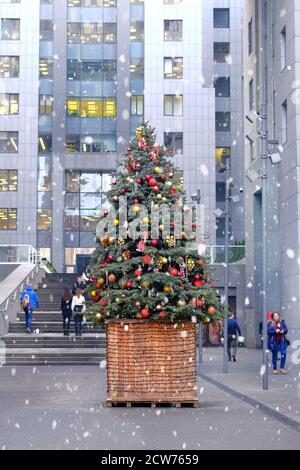 Arbre de Noël décoré de boules lumineuses et de supports de jouets devant l'entrée du centre de bureau. Neige dans la ville. Banque D'Images