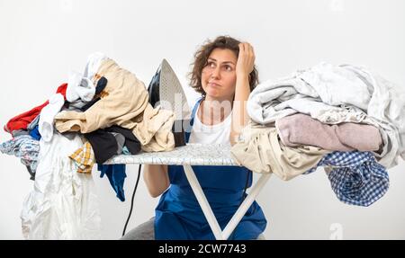 Une femme tient un fer dans ses mains et s'assoit à la table à repasser. Linge sale avant de repasser après le lavage. Concept de nettoyage, de lavage et de repassage Banque D'Images