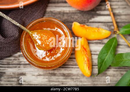 Confiture de pêche dans un pot en verre avec des quartiers de pêche et des fruits de pêche entiers. Confiture de pêche sur table en bois. Vue de dessus Banque D'Images