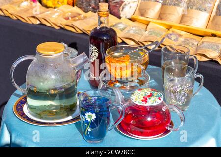 Théière en verre et tasses avec différentes sortes de tisanes sur la table dans un marché de rue Banque D'Images