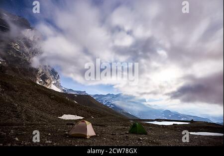 Paysage magique de ciel bleu ciel nuageux et étoiles brillantes, belle région de montagnes avec petits lacs. Magnifique crête de montagne avec hauts sommets rocheux, deux tentes touristiques colorées. Camping de nuit dans les Alpes Banque D'Images