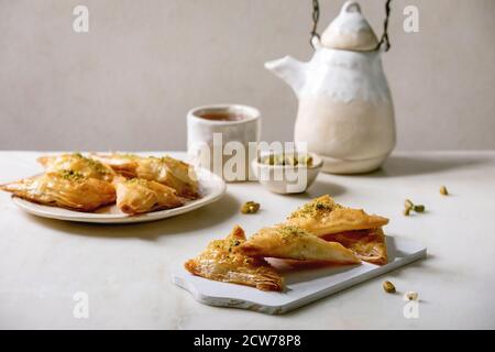 Baklava de dessert traditionnel turc maison avec pistache servie sur planche à découper en bois blanc avec bol de noix, tasse de thé, théière en céramique sur wh Banque D'Images