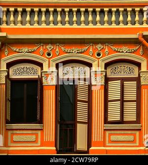 Un magasin peranakan chinois d'orange restauré avec des volets à persiennes en bois brun et des arches et des arcades ornées. Banque D'Images