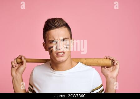 Homme énergique avec une batte sur un t-shirt à fond rose maquillage de visage lignes noires modèle d'agression Banque D'Images