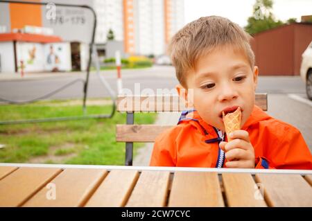 POZNAN, POLOGNE - 08 septembre 2020 : petit garçon caucasien polonais de trois ans qui mange de la crème glacée par une table en bois. Banque D'Images