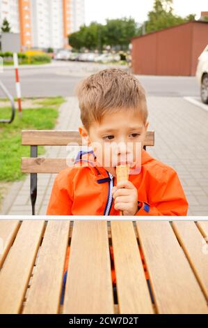 POZNAN, POLOGNE - 08 septembre 2020 : petit garçon caucasien polonais de trois ans qui mange de la crème glacée par une table en bois. Banque D'Images