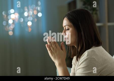 Profil d'une religieuse chrétienne priant lors d'une séance de nuit sur un canapé dans le salon à la maison Banque D'Images