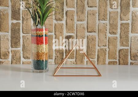 Pyramide de cuivre. Pyramide avec vase en verre et décoration de fleur artificielle avec pierres et fleurs multicolores, fond de mur de brique. Banque D'Images