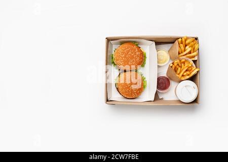 Déjeuner rapide moderne pour deux. Hamburger et cheeseburger, ketchup et sauce dans des récipients, frites dans des sacs en papier et tasse de café dans une boîte Banque D'Images