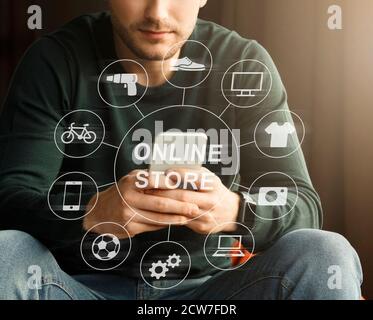 Shopping sur Internet. Jeune gars parcourant la boutique en ligne, collage avec des icônes de différents produits sur l'écran virtuel Banque D'Images
