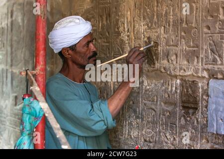 Un homme à l'aide d'un pinceau travaille sur la restauration d'une section de hiéroglyphes sculptés dans un mur de pierre au temple de Karnak à Louxor en Égypte. Banque D'Images