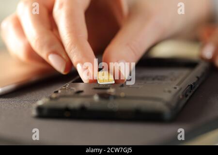 Gros plan des mains de femme mettant la carte sim sur le smartphone sur un bureau Banque D'Images