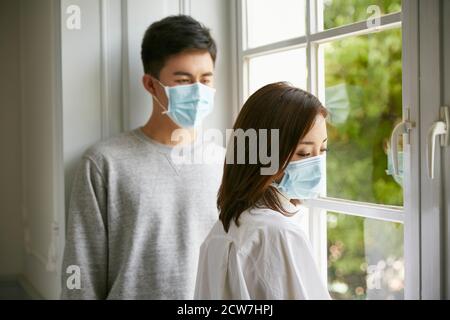 jeune couple asiatique isolé portant un masque debout près du fenêtre Banque D'Images