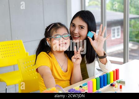 Bonne fille avec le syndrome de Down et l'enseignant jouer jouet puzzle dans la salle de classe. Concept d'apprentissage des enfants handicapés à l'école. Banque D'Images