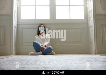 jeune femme asiatique en quarantaine à la maison assise sur le sol jambes crosedd portant un masque facial Banque D'Images