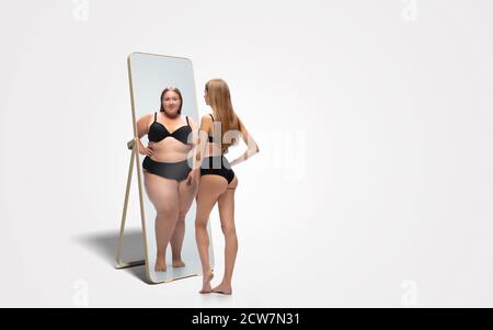 Jeune femme mince, en forme de femme regardant la grosse fille dans le miroir de réflexion sur fond blanc. Pensant qu'elle n'est pas assez sportive. Concept de mode de vie sain, forme physique, sport, nutrition et corps positif. Banque D'Images