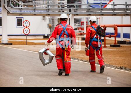 Raffinerie de pétrole et usine de traitement du gaz. Deux grimpeurs industriels en vêtements de travail rouges et casques blancs. Gisement de pétrole de Zhaik-Munai, Kazakhstan. Banque D'Images