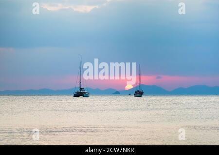 Trois yachts à voile dans la mer. Au coucher du soleil, le soleil se couche sur les montagnes. Banque D'Images