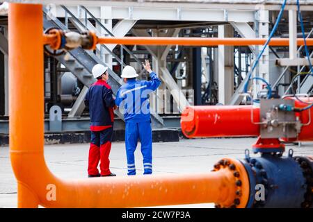 Gisement de pétrole de Zhaik-Munai, Kazakhstan. Usine de raffinage de pétrole. Deux ingénieurs ou travailleurs du pétrole dans le bleu de travail portent et casques blancs discutant quelque chose. Banque D'Images