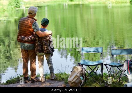 Portrait de père et de fils debout au bord du lac et profitant de la nature pendant la randonnée ou la pêche, espace de copie Banque D'Images