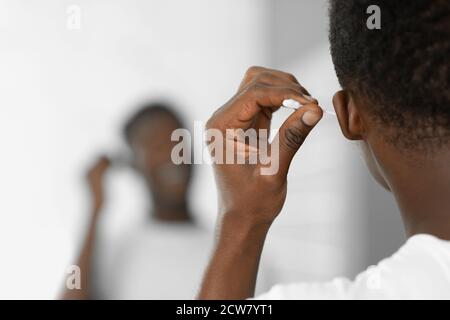 Homme noir nettoyer les oreilles à l'aide d'un coton-tige debout dans la salle de bains Banque D'Images